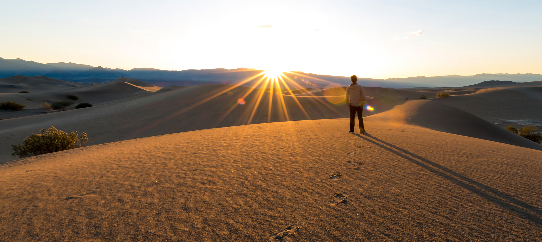 Man Standing And Looking At The Sunrise In The Desert