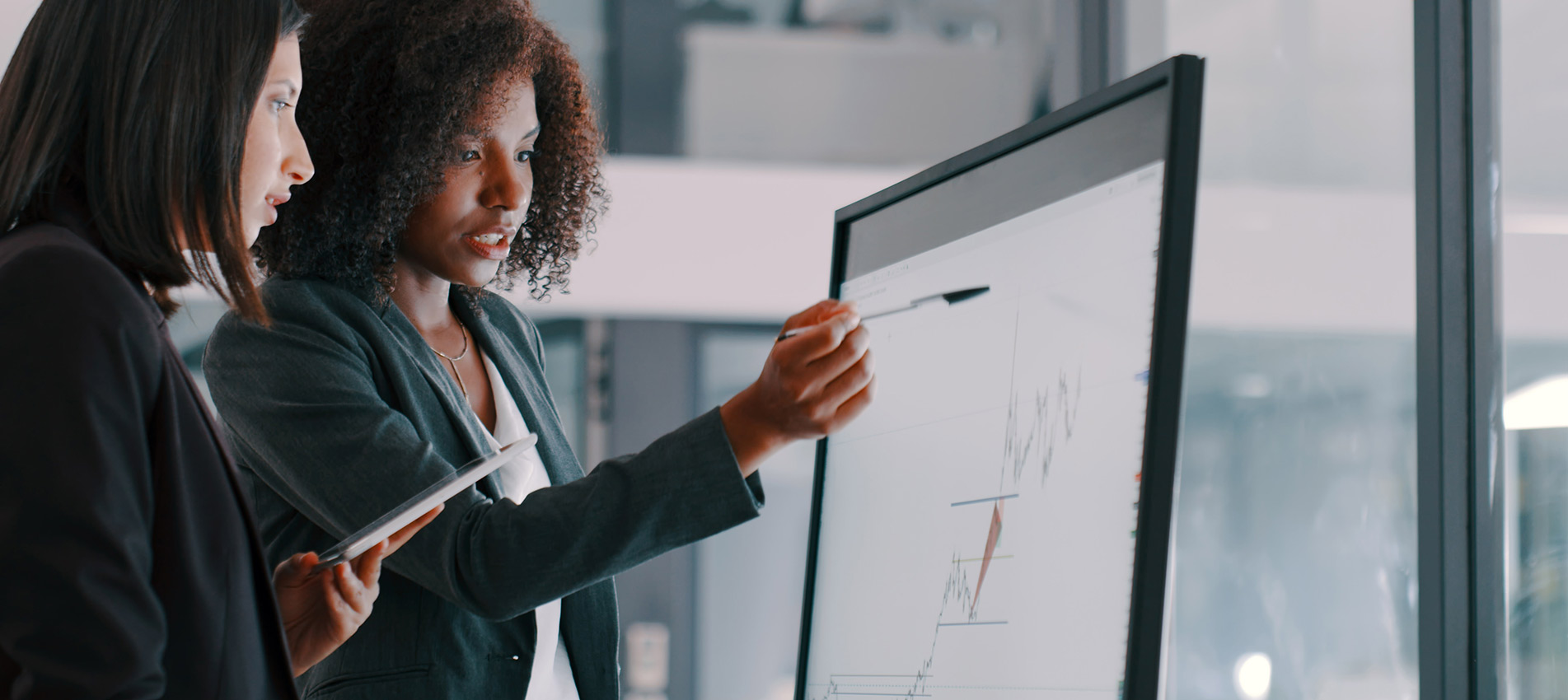Two Young Businesswomen Using An Interactive Whiteboard To Analyse Data In A Modern Office