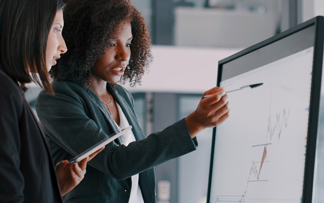 Two Young Businesswomen Using An Interactive Whiteboard To Analyse Data In A Modern Office