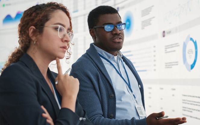 Black Man And Hispanic Woman Working On Business Strategy And Standing Infront Of Big Digital Screen With Data