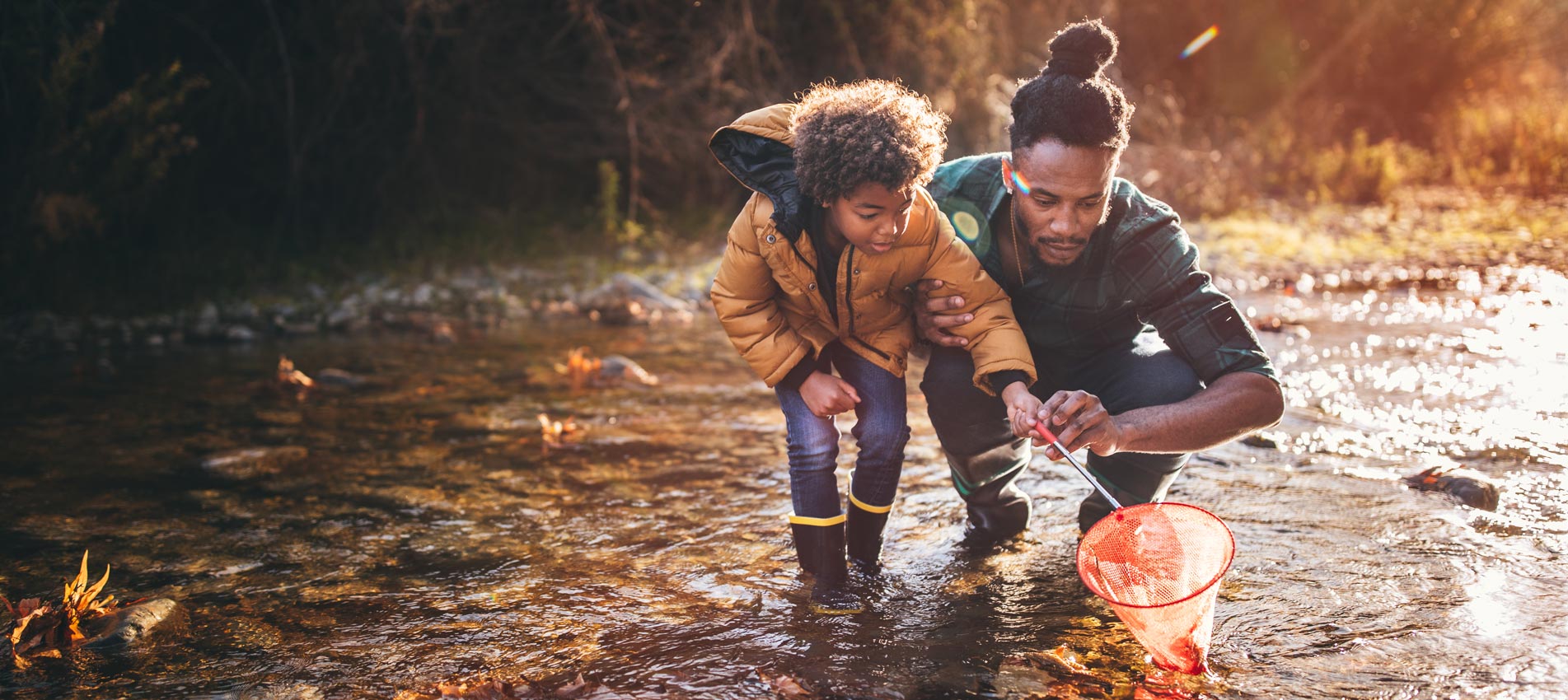 African American Father And Son Fishing With Fishing Net In River