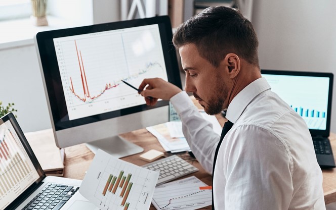 Young Businessman Comparing Data Using Computer At The Office